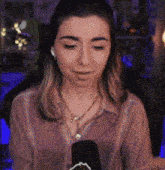 a woman wearing headphones and a necklace is holding a microphone in front of her face .