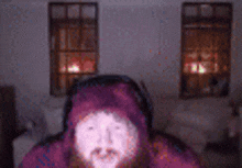 a man with a beard is wearing a purple hoodie and headphones in a living room .