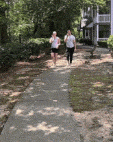 two people walking down a sidewalk in front of a white house