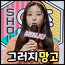 a woman is holding a microphone in front of a colorful background with korean writing on it .