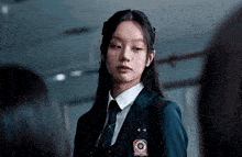 a girl in a school uniform and tie is standing in a dark room .