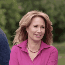a woman in a pink shirt and necklace is smiling