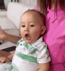 a woman is holding a baby in her arms and the baby is wearing a green and white shirt .