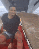 a man in a black shirt is sitting on a red boat in the water