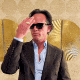 a man in a suit and sunglasses holds his hand to his head