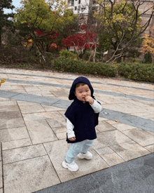 a baby wearing a black poncho with a hood is standing on a sidewalk