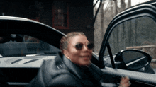 a woman wearing sunglasses is getting out of a black car