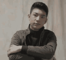 a young man with his arms crossed is wearing a jacket and a turtleneck .