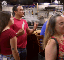 a man in a red shirt is talking to two women in front of a paramount network sign