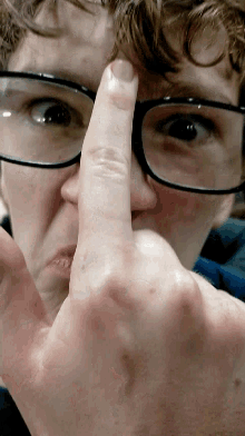 a close up of a person 's face with glasses and a finger on their nose