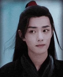 a young man with long black hair and a red ponytail looks at the camera