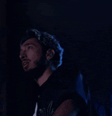 a man with a beard is standing in a dark room with a blue light behind him .