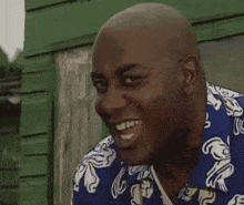 a bald man wearing a blue shirt is smiling in front of a green building .