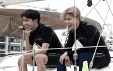 two men wearing wet suits are sitting on a boat and one of them is wearing the word wave