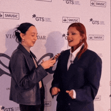 two women are standing in front of a wall that says smusic on it