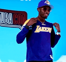 a man wearing a lakers shirt stands in front of a sign that says nba con
