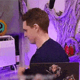 a man in a blue shirt is sitting in front of a laptop with a sticker of a man holding a sword on it