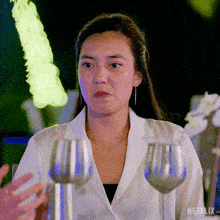 a woman in a white shirt is standing in front of two wine glasses with netflix written on the bottom right