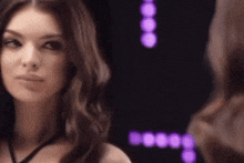 a woman is looking at herself in a mirror with purple lights in the background .