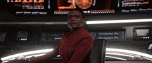 a woman in a red jacket is sitting in front of a monitor that says ' a ' on it