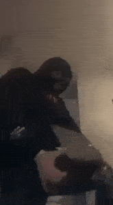 a man in a ski mask is standing in a room holding a laptop .