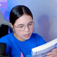 a woman wearing glasses and a blue shirt is reading a book called deeply