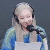 a woman wearing headphones is sitting in front of a microphone and reading a piece of paper .