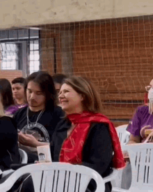 a woman in a red scarf is smiling while sitting in a chair in front of a group of people .
