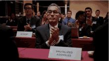 a man sits at a table with a sign that says brutalized assholes on it