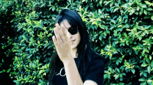 a woman wearing sunglasses and a patch on her eye is standing in front of a bush