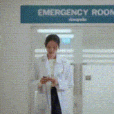 a doctor is standing in front of an emergency room looking at her phone .