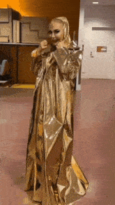 a woman in a long gold coat is standing in a hallway .