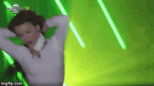 a woman in a white sweater is dancing in front of green lights