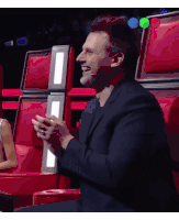 a man in a suit is smiling while sitting in a row of red seats