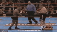 two men are fighting in a boxing ring with a referee standing between them .