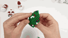 a person is holding a christmas tree made of green and white beads