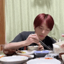 a young man with red hair is sitting at a table eating food with chopsticks