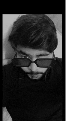 a man wearing sunglasses and a black shirt looks at the camera