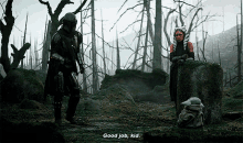 a man and a woman are standing in a forest talking to a baby yoda .