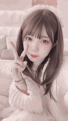 a girl wearing a headband and a white sweater is giving a peace sign