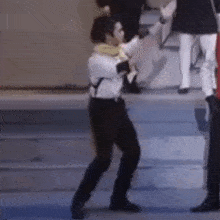 a man in a white shirt and black pants is dancing on a stage with a group of people .