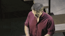 a man in a red shirt is standing on a stage in front of a staircase .