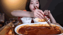 a woman is using chopsticks to eat a large bowl of soup