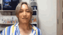a man wearing a blue and yellow striped shirt is smiling in front of a bookshelf .