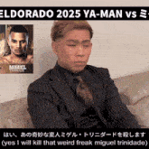 a man in a suit is sitting on a couch with a poster of miguel trindade behind him