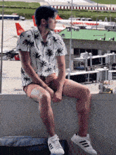 a man in a palm tree shirt sits on a wall
