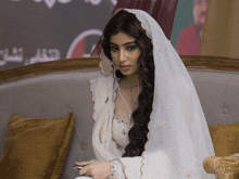 a woman in a white veil sits on a couch with a phone in her hand