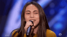 a young woman is singing into a microphone on nbc 's america 's got talent .