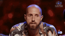 a bald man with a beard is wearing a floral shirt and looking at the camera .
