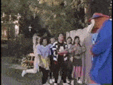 a group of people are standing in front of a fence while a clown stands behind them